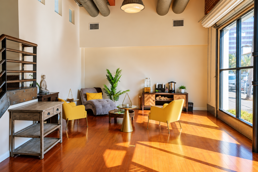 The real DE SUAR Hollywood lounge with yellow chairs, warm wood floors and tall windows
