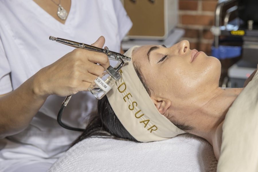 An esthetician performing a facial mist treatment on a guest wearing a DE SUAR headband